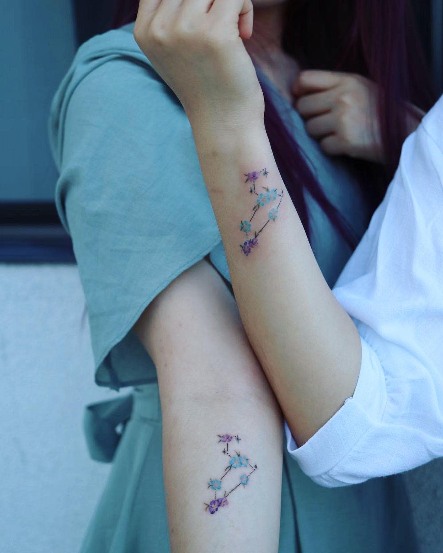 Two arms with matching delicate flower constellation tattoos